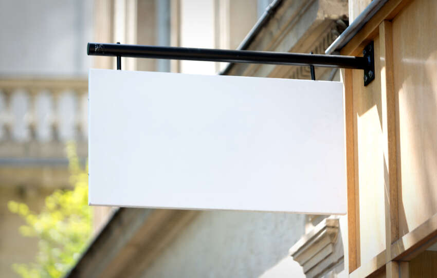 Blank store sign hanging outside a shop, representing the concept of choosing store names. Feature image for a blog titled '100+ Store Names for Your Business.'