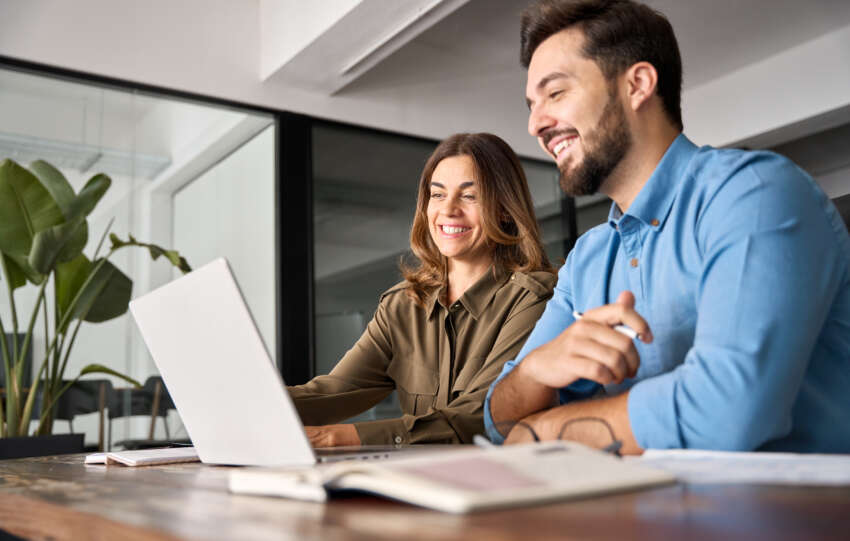 How to Register a Business: Two smiling professional business people talking using a laptop.
